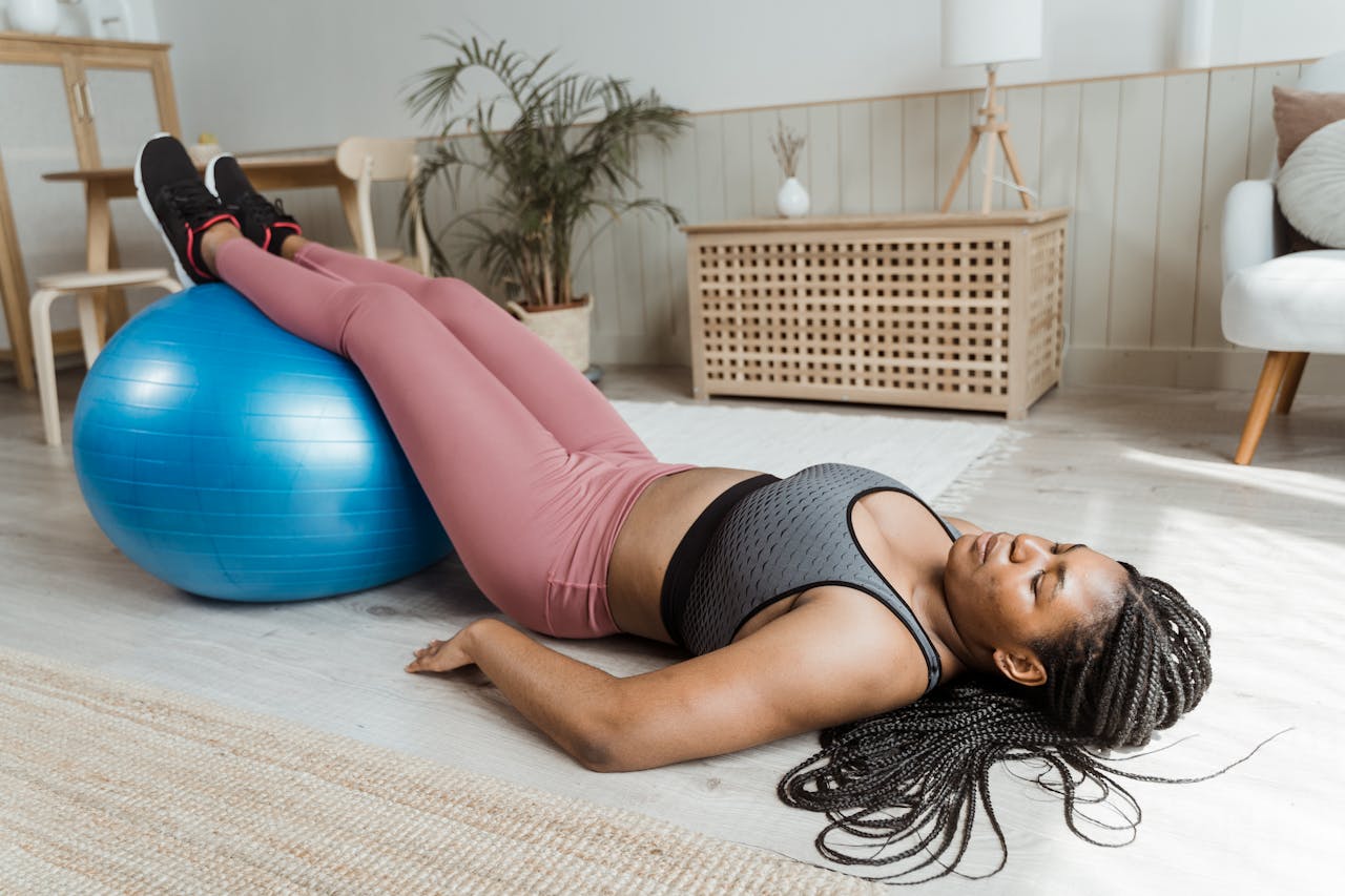 African American woman lying on gym ball in home setting, focusing on fitness and relaxation.